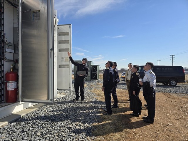 A technician shows open battery equipment cabinets to a visiting Singapore Armed Forces delegation at Fort Detrick