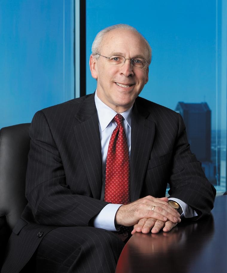Craig Morrison seated at a table in a dark suit and red tie, with blue windows behind him