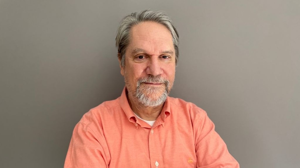 Craig S. Smith in an orange shirt, seated against a gray background