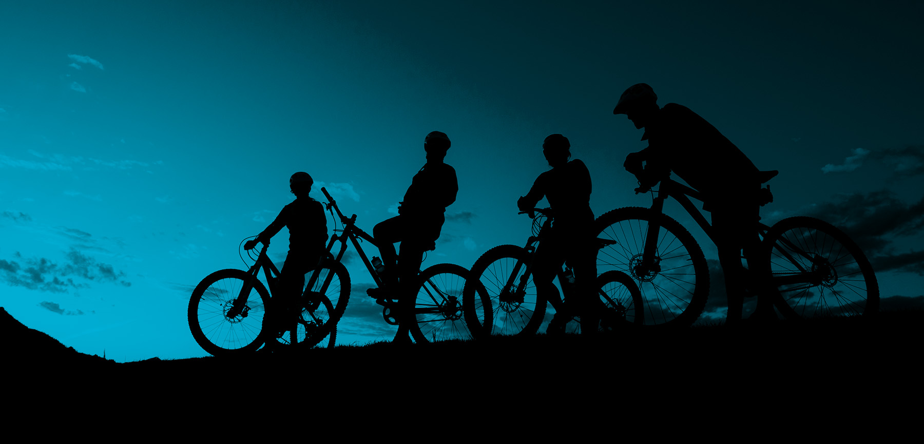 Four mountain bikers silhouetted against a teal evening sky