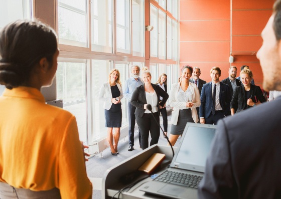 People gathered around presenters and a laptop in a bright event space