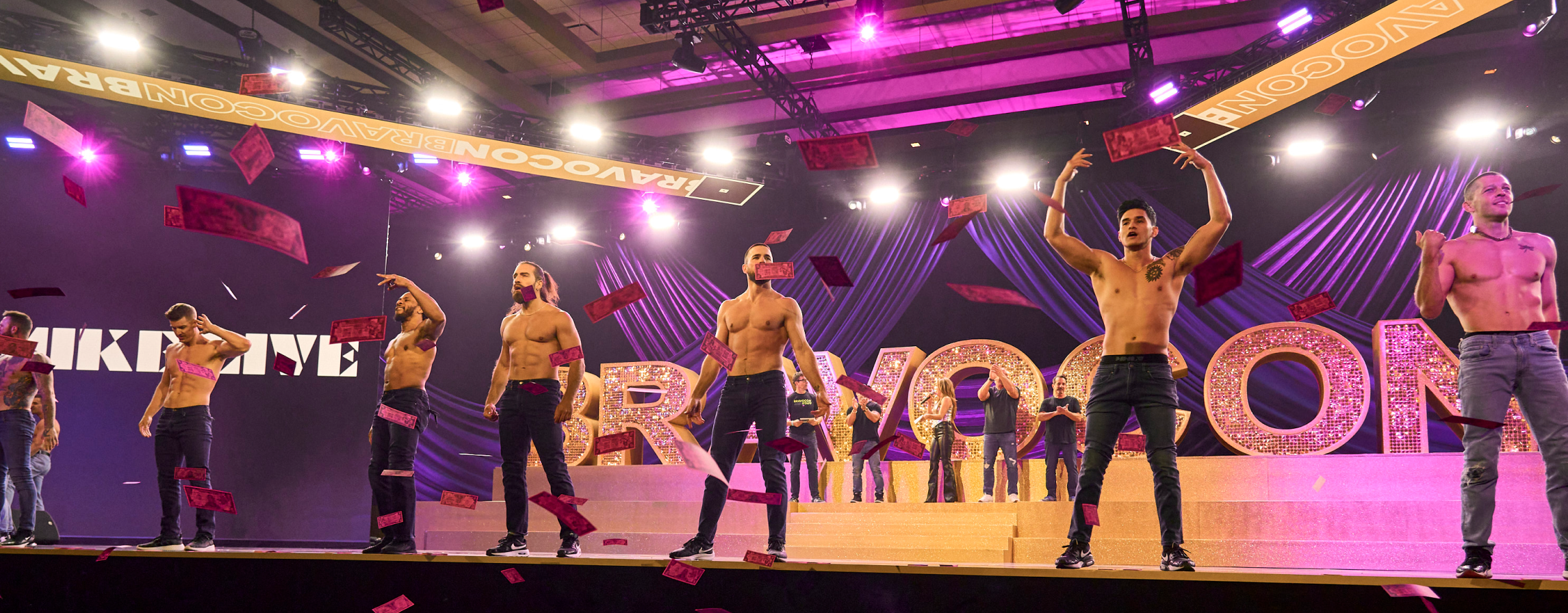 Performers on a brightly lit BravoCon stage as pink paper flies through the air