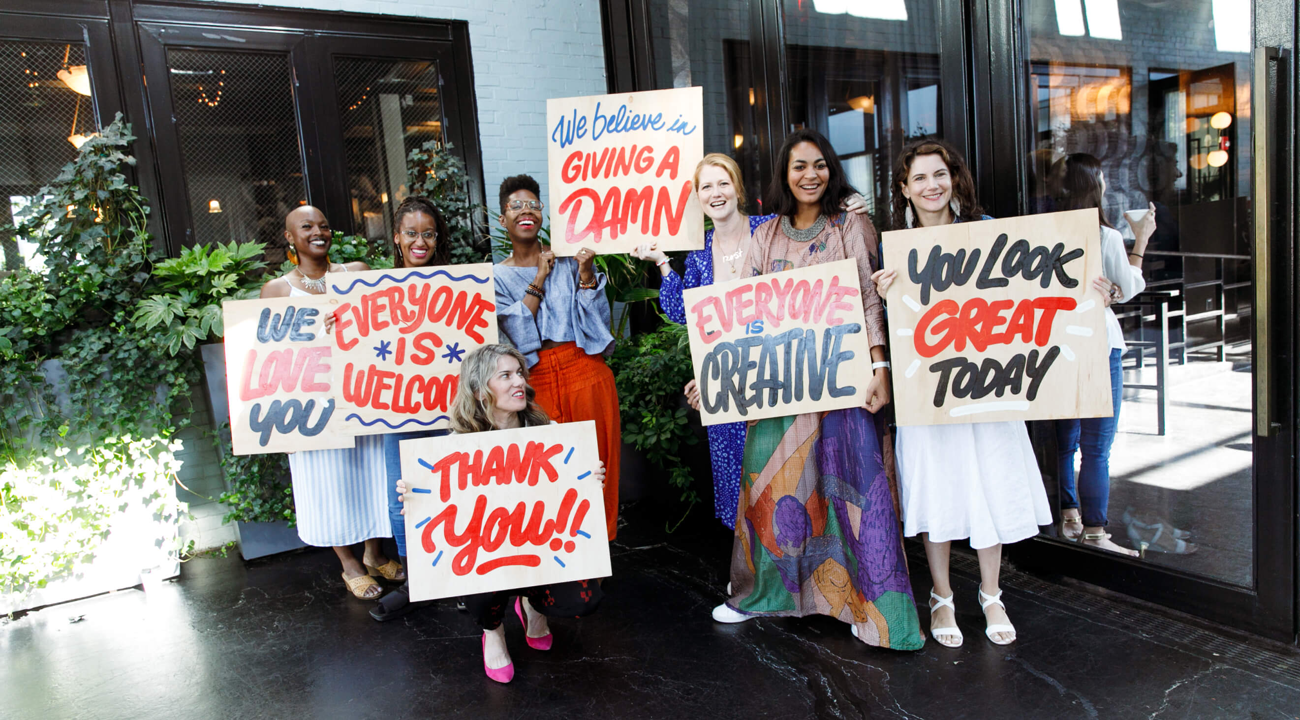 CreativeMornings community members holding hand-painted signs about creativity and welcome