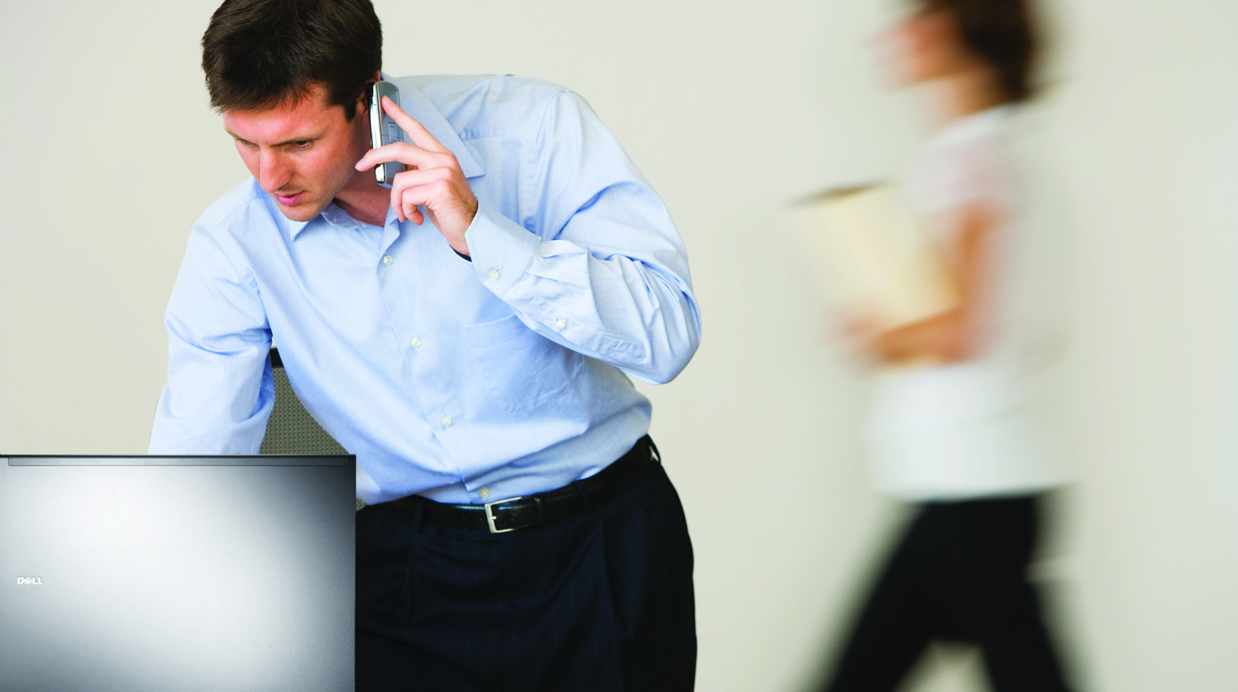 Period Dell promotional photograph of a worker using a phone beside an open Dell laptop