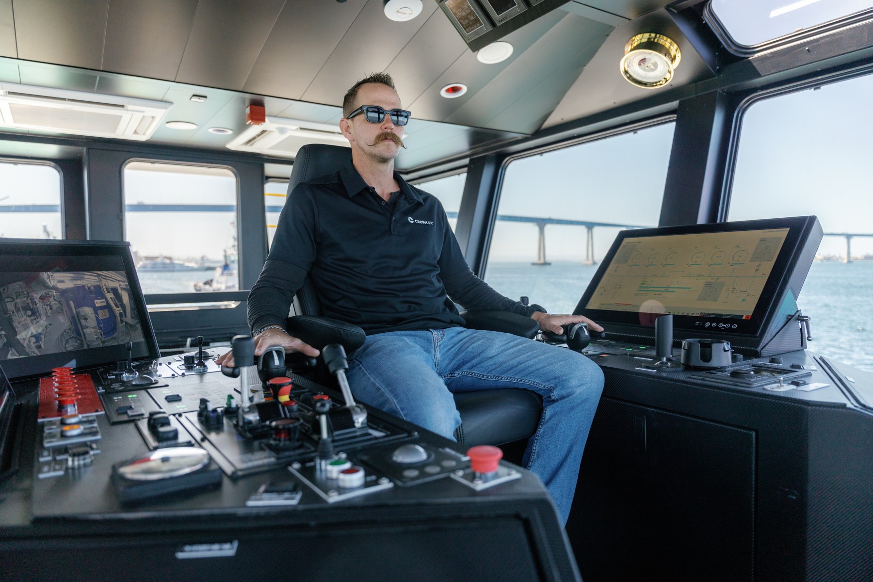 A Crowley mariner seated at eWolf’s wheelhouse controls, surrounded by screens and windows.