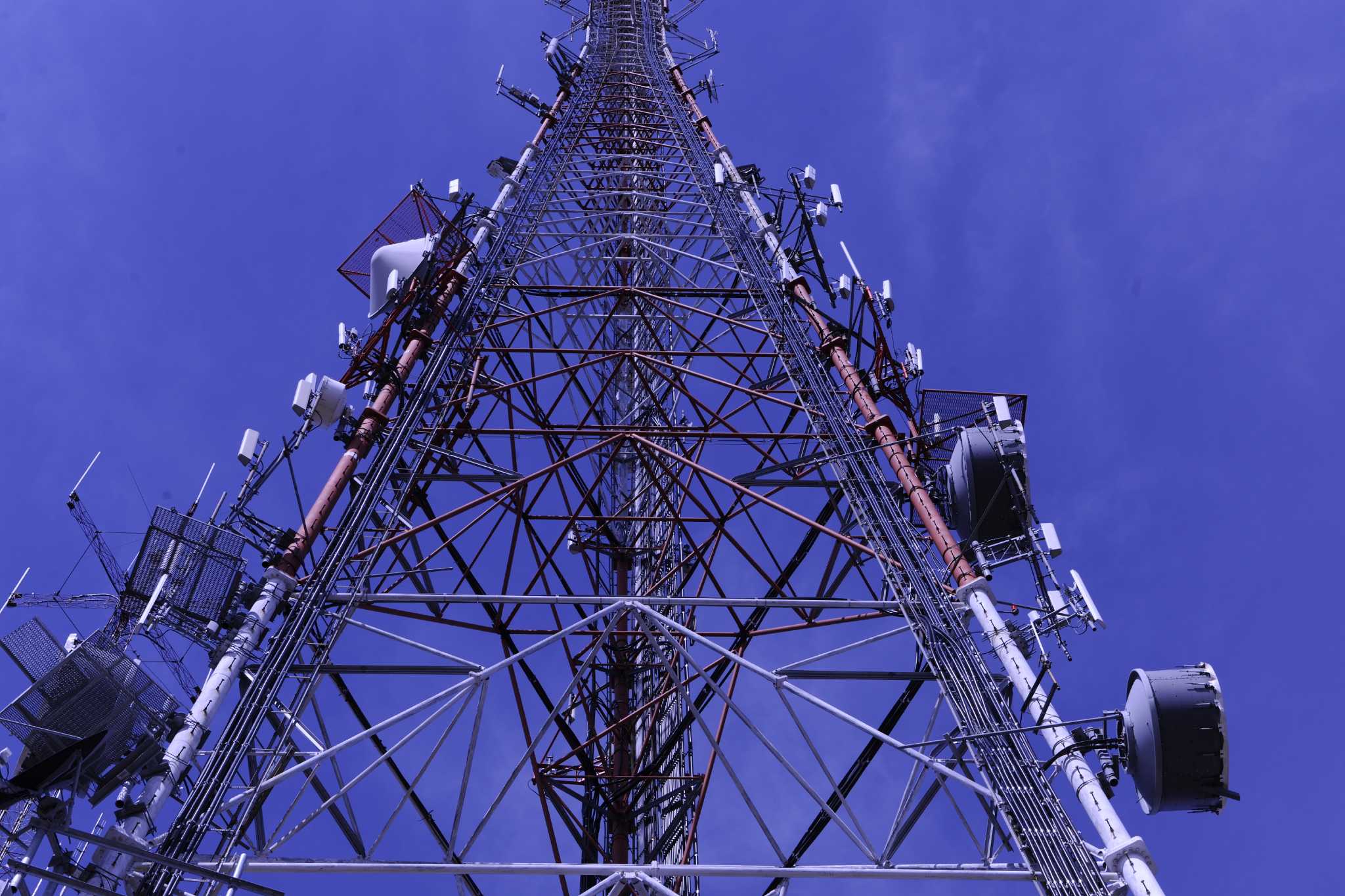 Crown Castle lattice communications tower carrying antennas and microwave dishes against a blue sky
