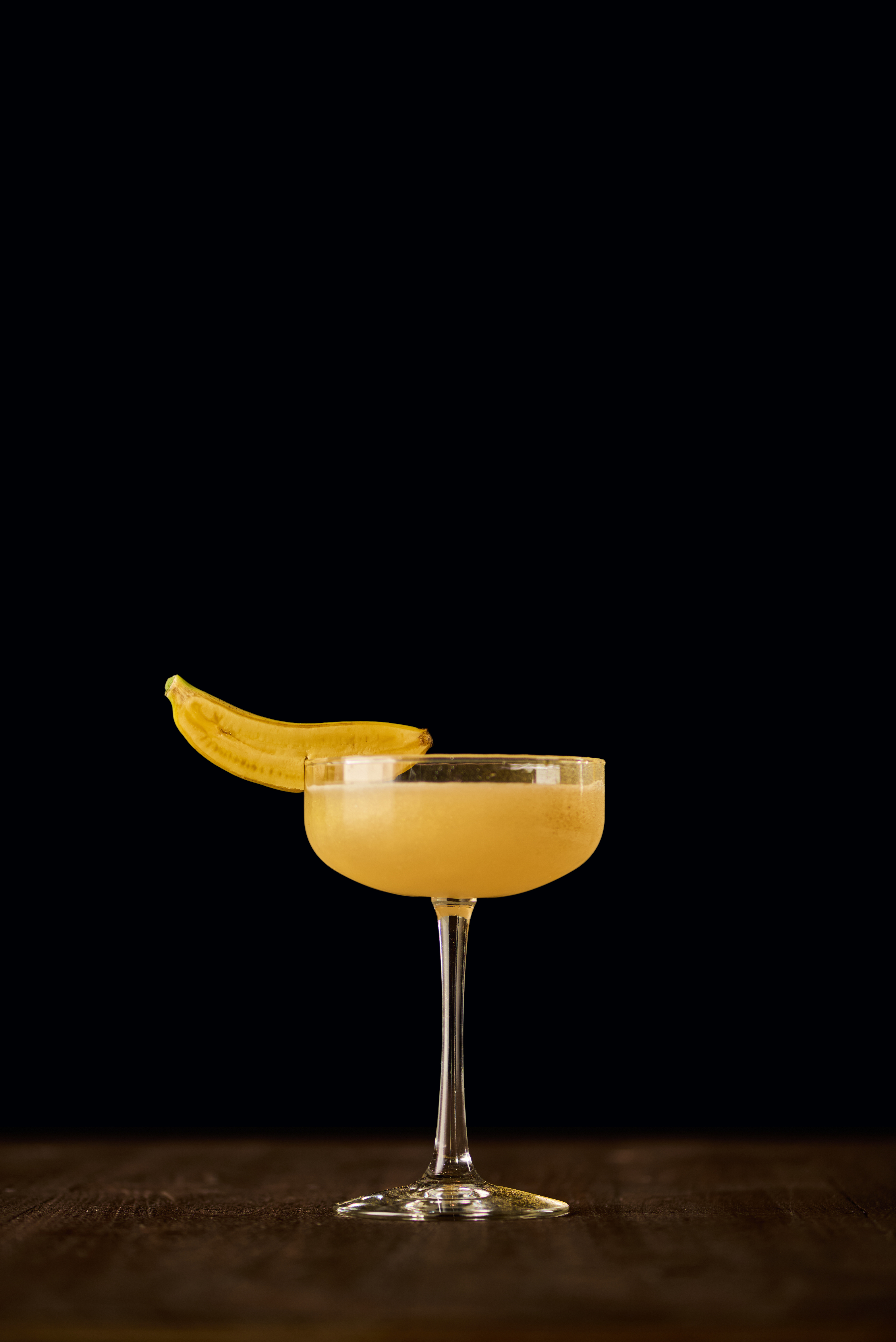 A banana daiquiri in a coupe against a black background