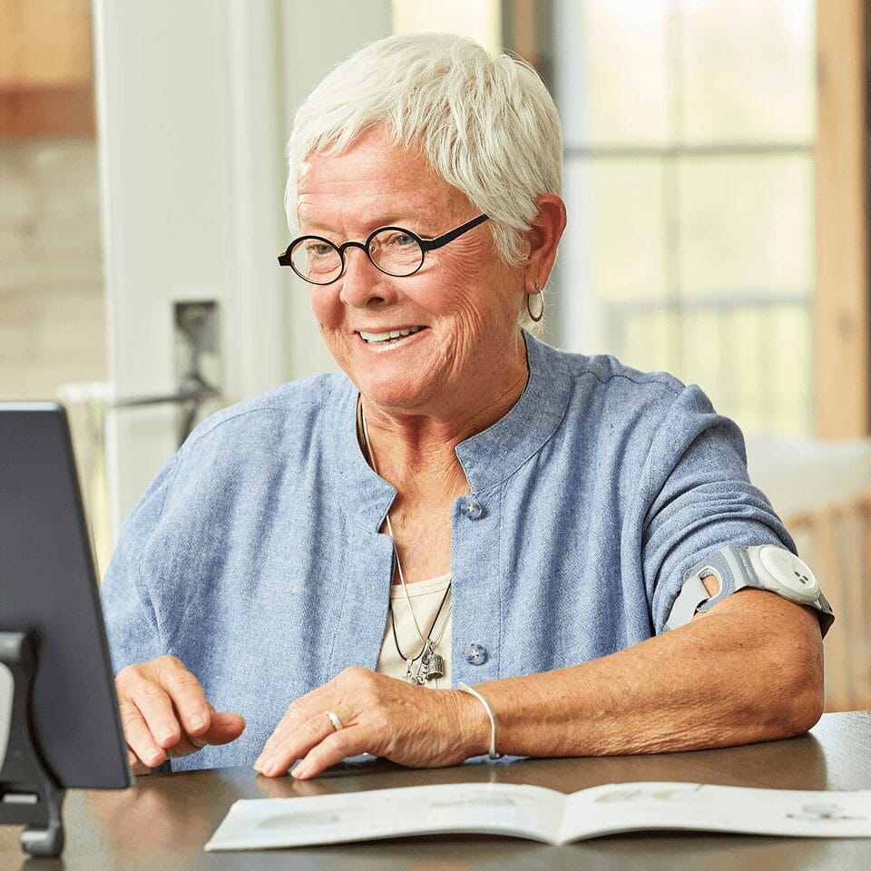 A patient at home wearing a Current Health monitoring device while using a tablet
