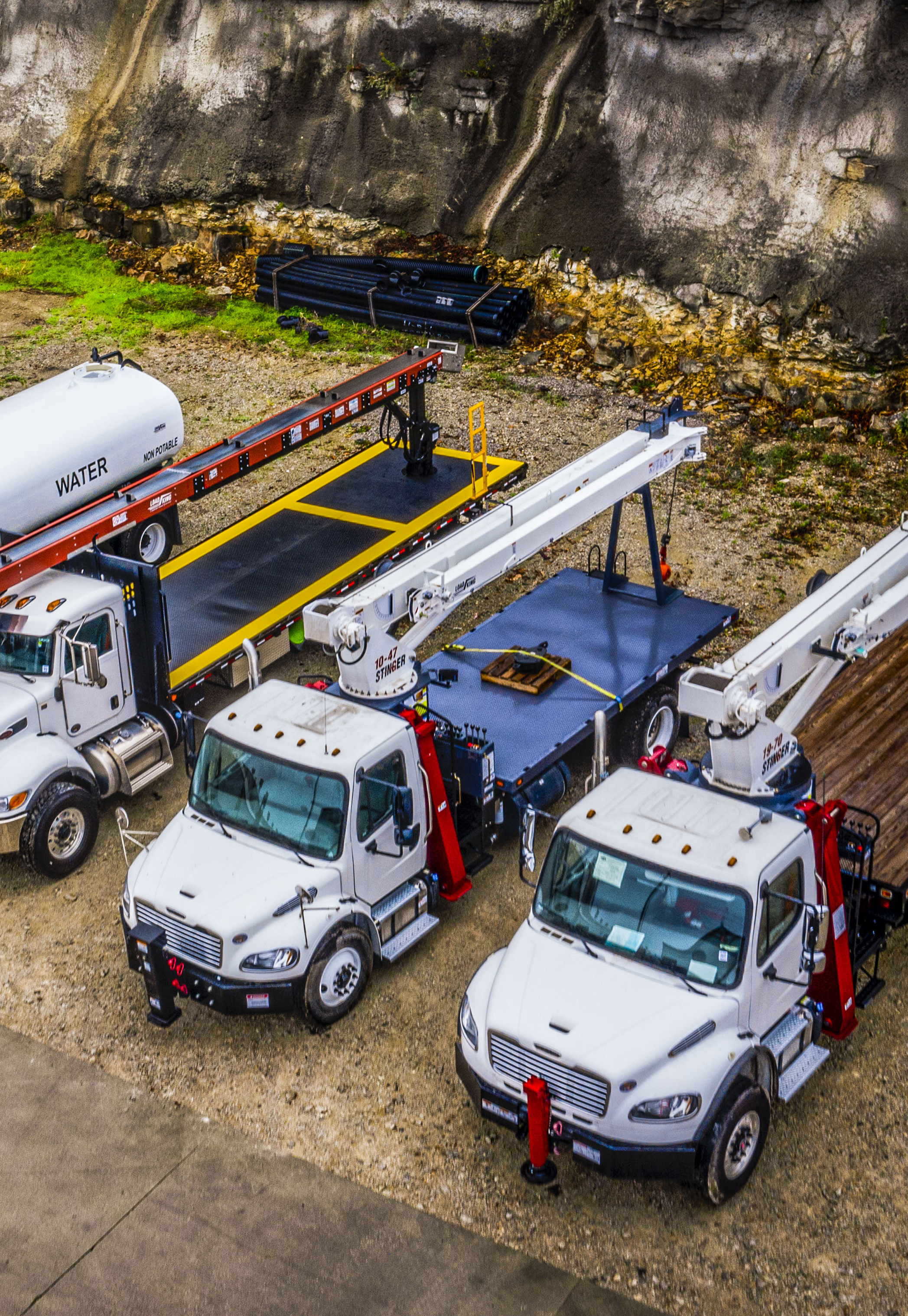 White work trucks fitted with Load King Stinger cranes parked beside other vocational equipment
