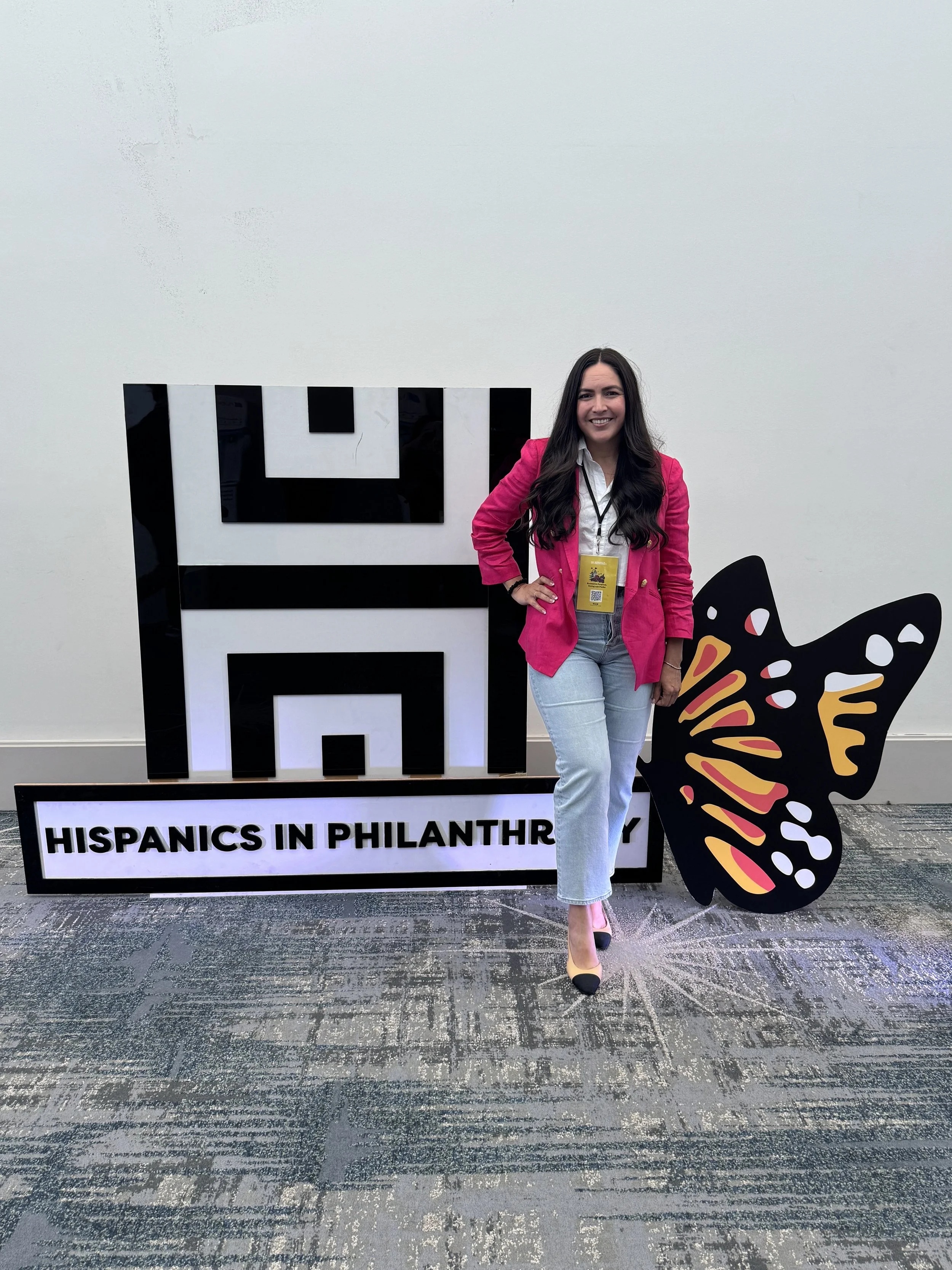 Daisy Sayre Garcia in a pink jacket beside Hispanics in Philanthropy conference lettering