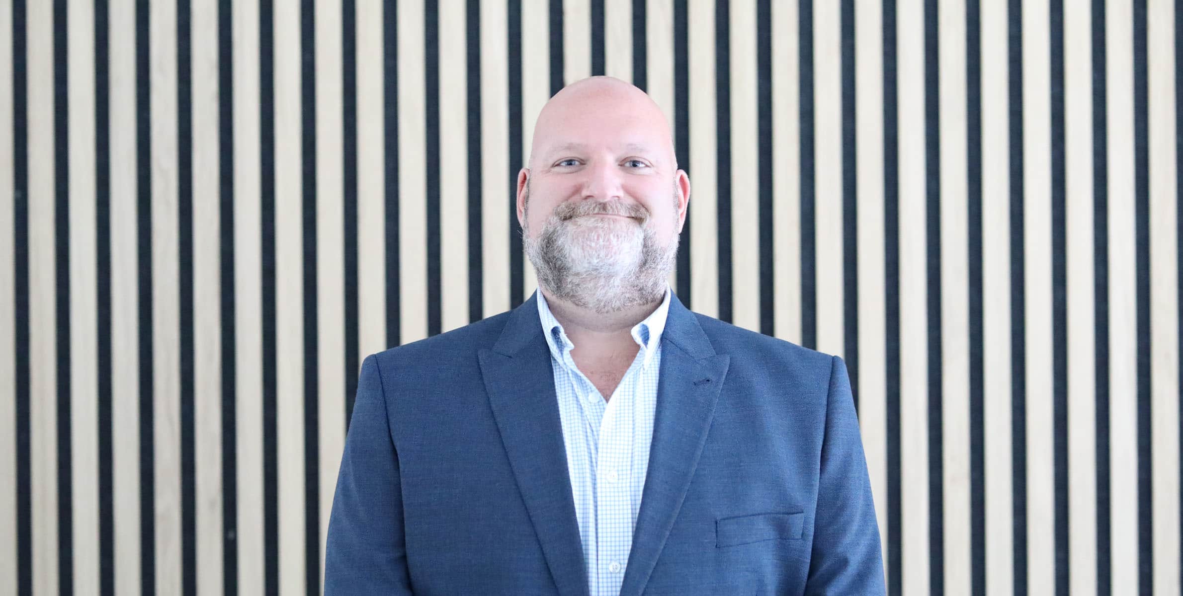 Andrew Hay, Chief Operating Officer of Damovo, standing in front of vertical wooden slats
