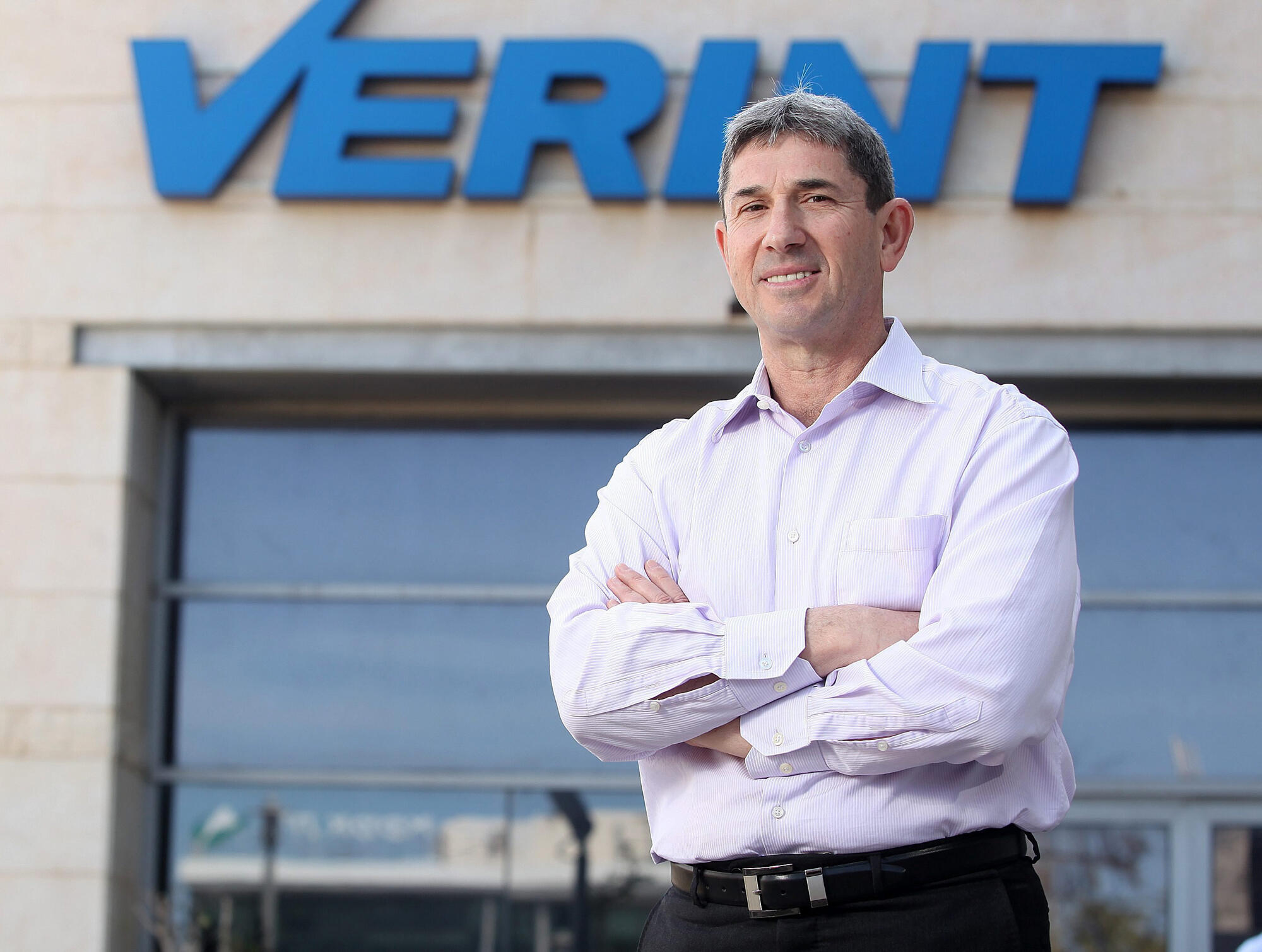 Dan Bodner in a light purple shirt, standing outside a building beneath the Verint sign