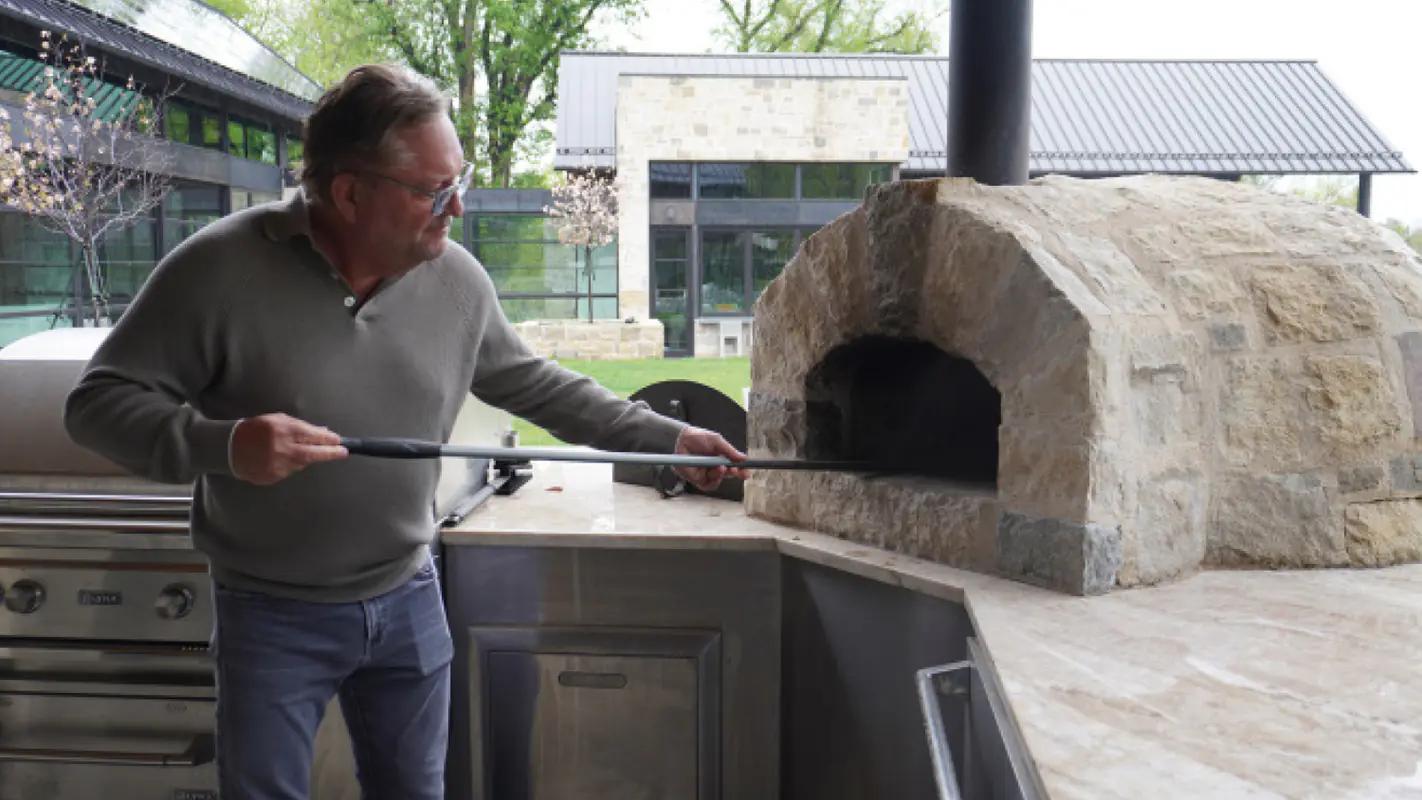 Dan Caruso using a long pizza peel at his outdoor stone pizza oven