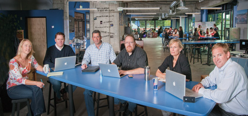 Six members of G5’s early team at a table with laptops; Dan Hobin is seated at far right.