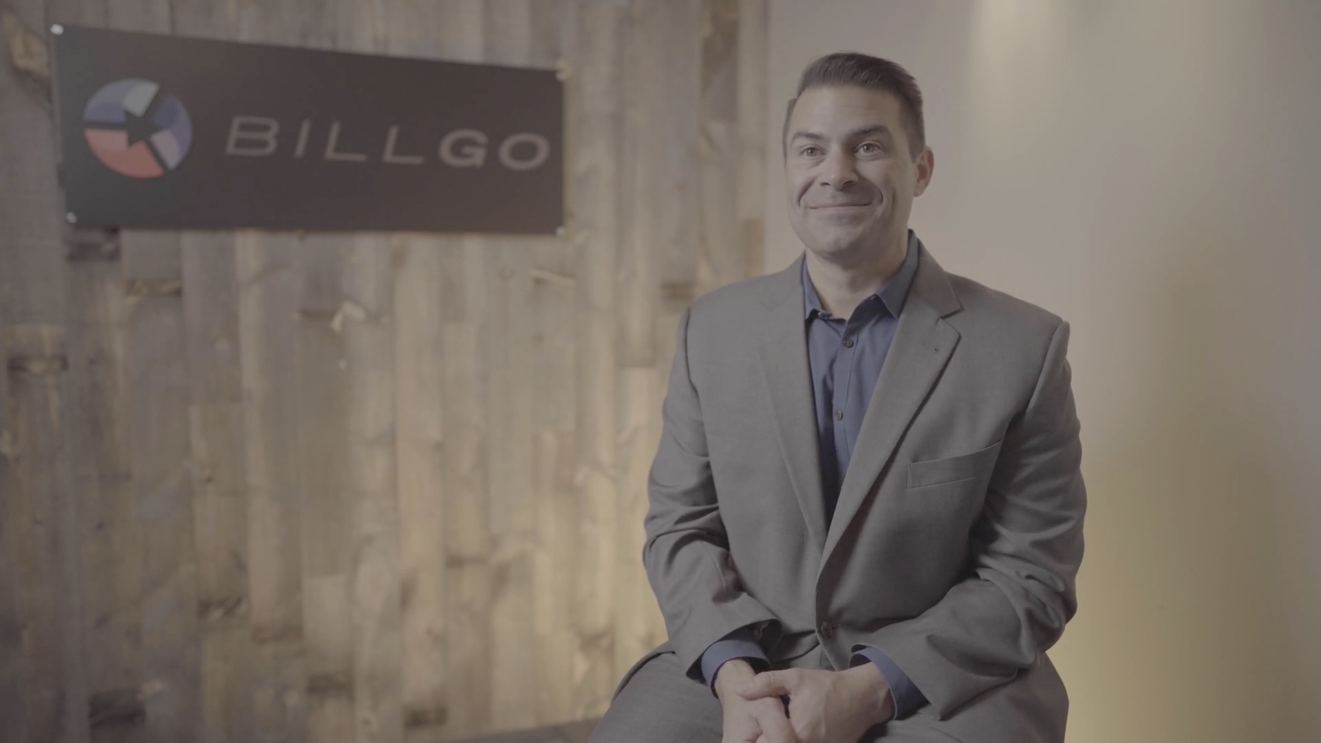 Dan Holt seated beside a BillGO sign in a wood-paneled office