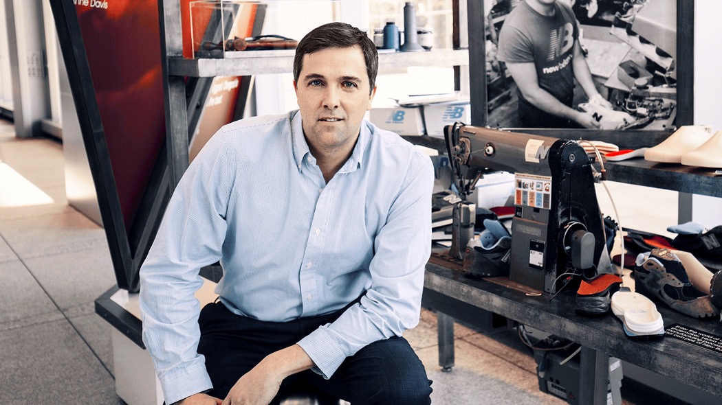 Dan McKinnon seated beside a sewing machine and a footwear workbench at New Balance