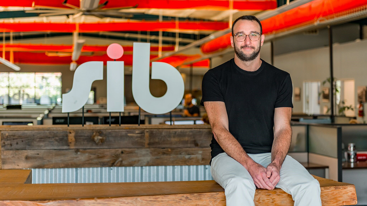 Dan Schneider seated inside an SIB office, beside the company’s lettering and exposed red ductwork