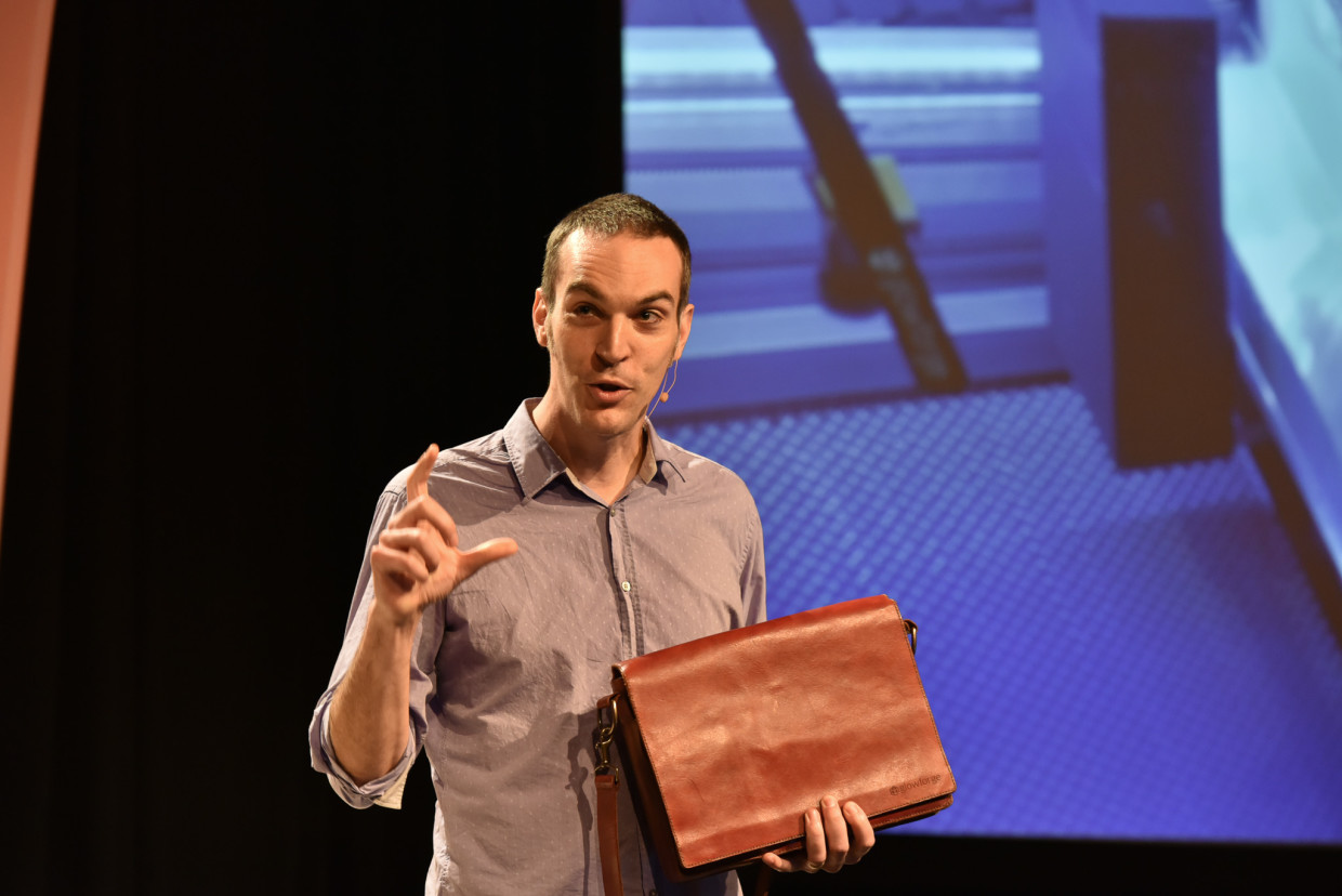 Dan Shapiro speaking onstage while holding a leather case made with a Glowforge