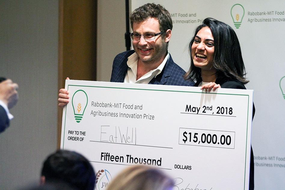 Dan Wexler and Priya Patel smiling while holding EatWell’s $15,000 prize check at MIT in May 2018