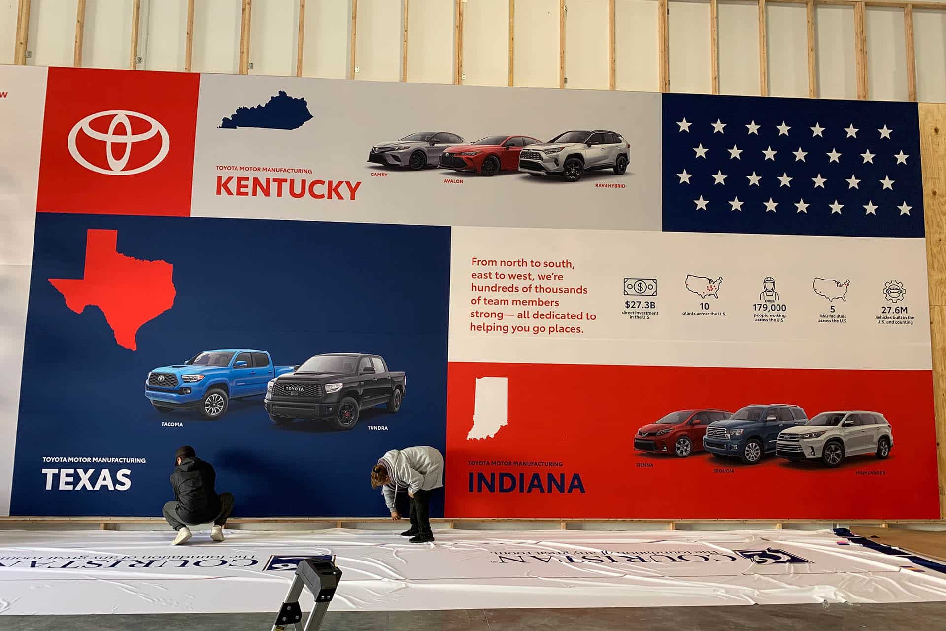 Two DVC workers fit a large Toyota fabric graphic against the workshop test wall