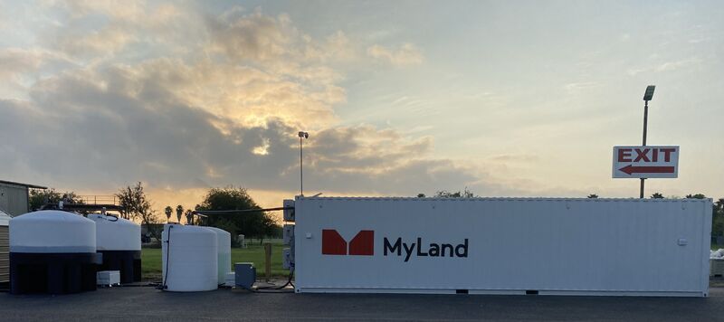 A white MyLand installation and adjacent tanks beneath a clouded Texas sky