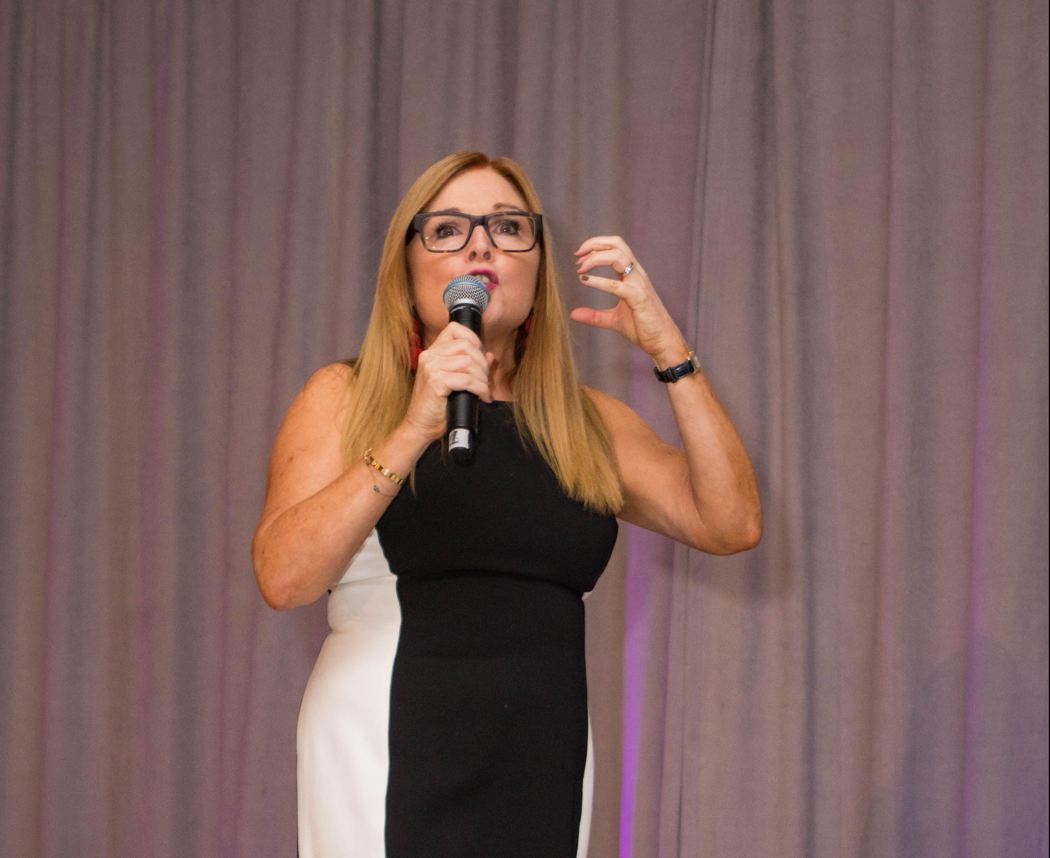 Danica Kombol speaking into a handheld microphone onstage