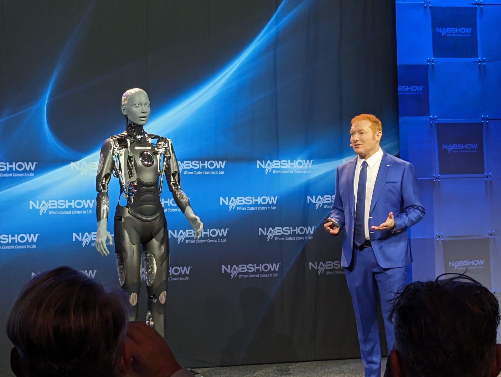 Daniel Anstandig speaking beside the humanoid robot Ameca on the NAB Show stage