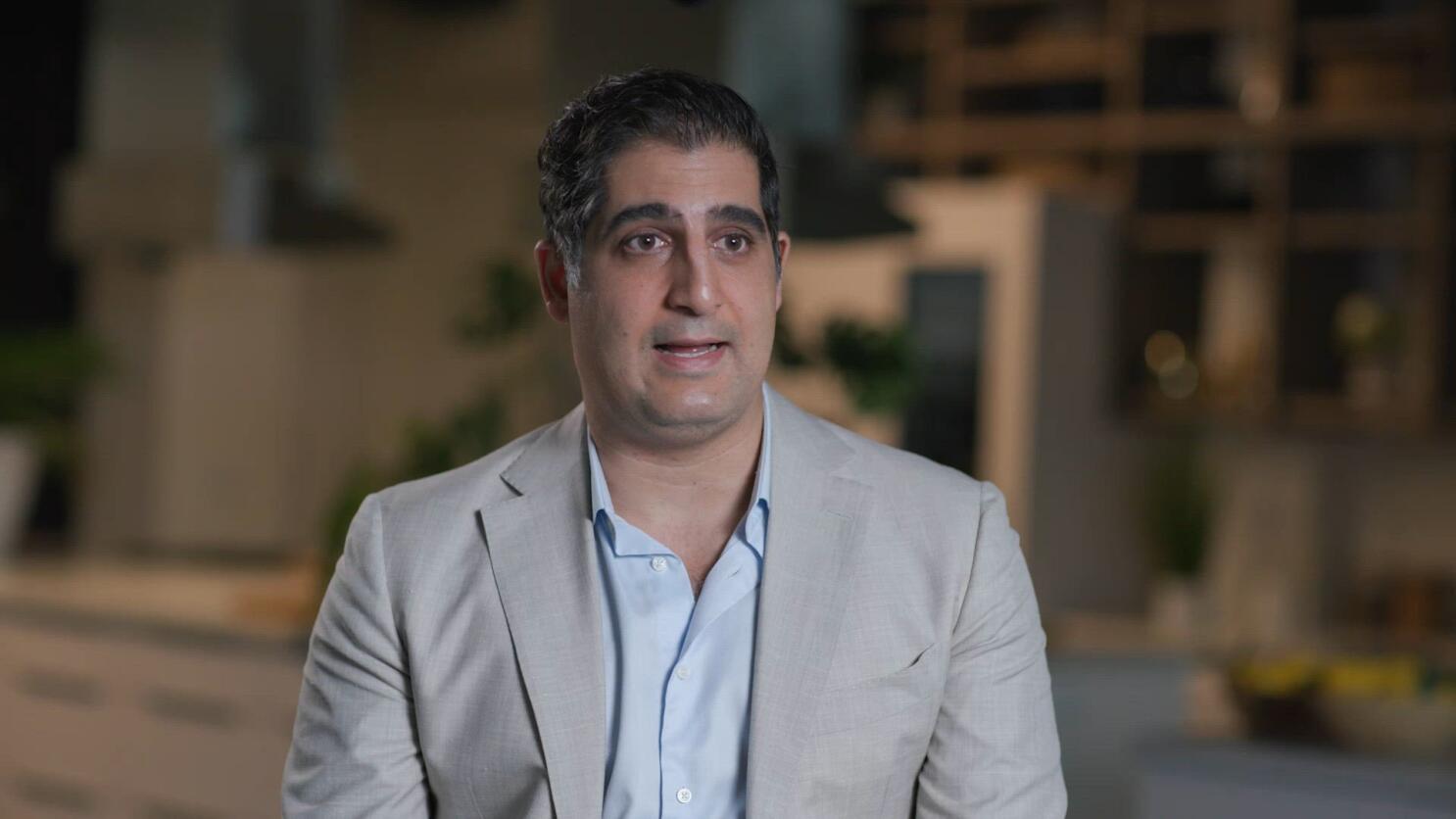 Daniel Broukhim seated during an interview, wearing a light gray jacket and blue shirt
