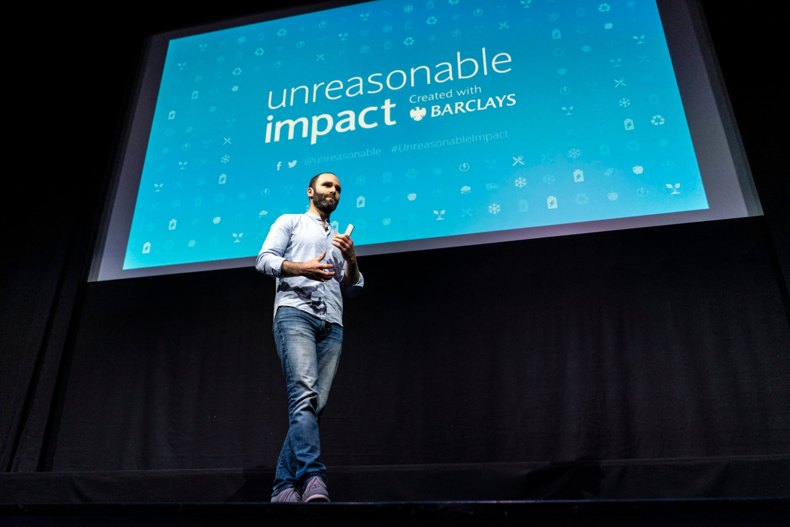 Daniel Epstein speaking onstage in front of the Unreasonable Impact and Barclays screen