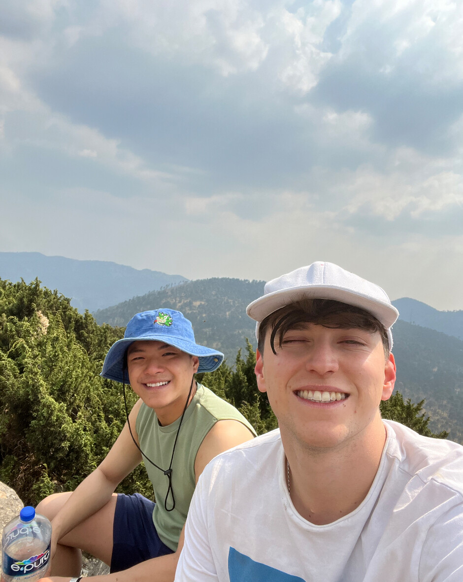 Justin Zhou, left, and Danny Bessonov, right, smiling outdoors in hats with mountains behind them