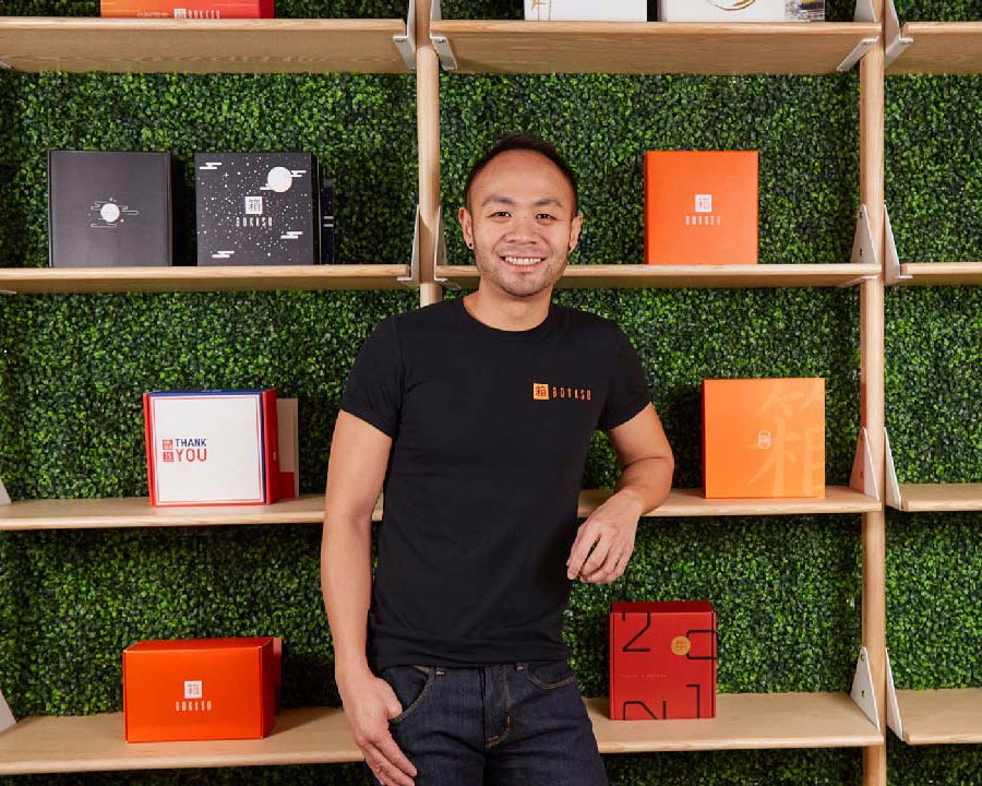 Danny Taing standing beside shelves of colorful Bokksu boxes