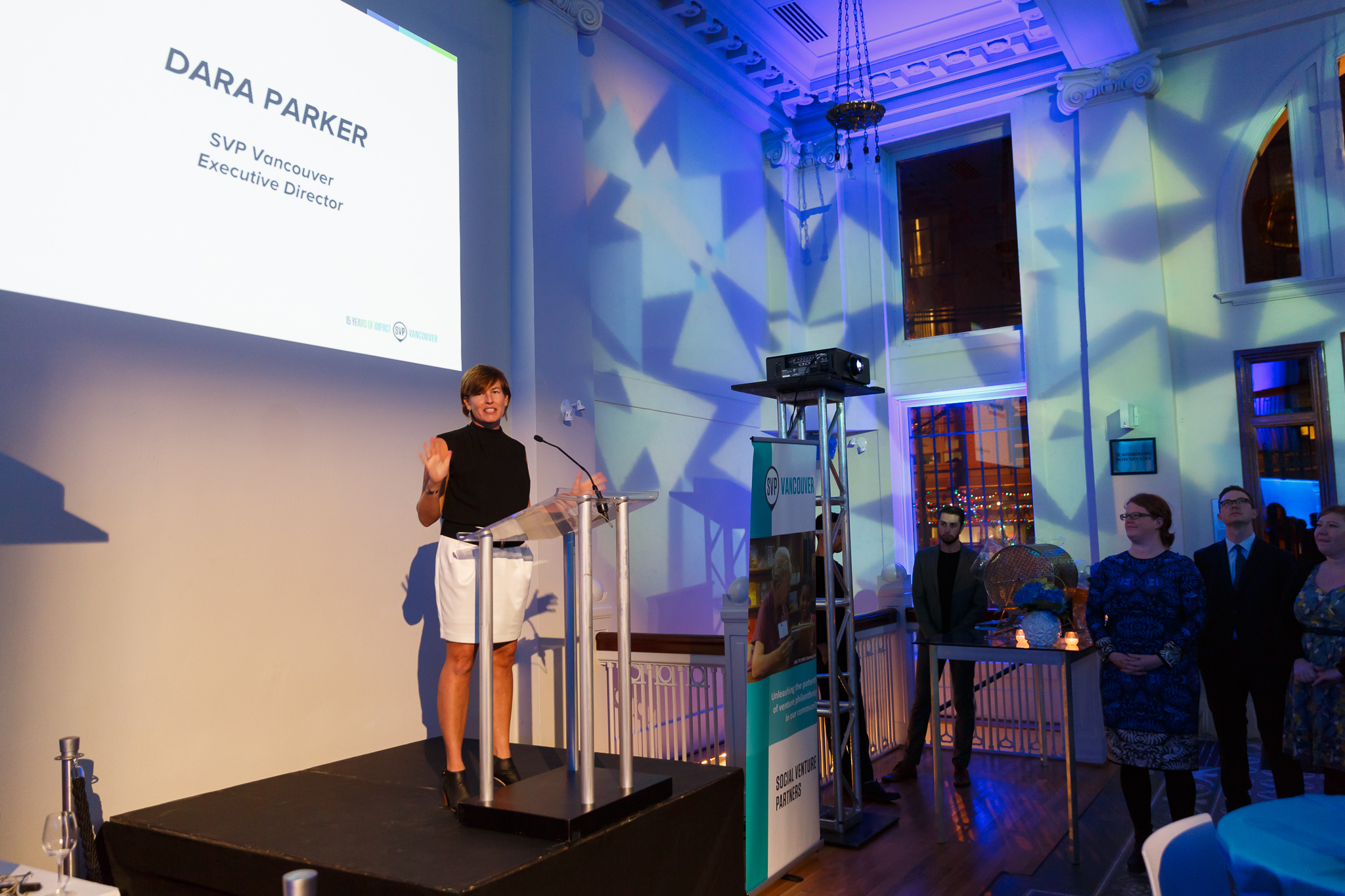 Dara Parker speaking at a lectern with a screen identifying her as SVP Vancouver executive director