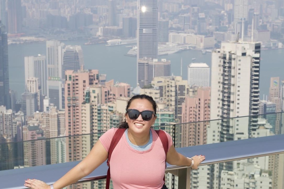 Darcy Palder smiling at a viewpoint overlooking Hong Kong’s buildings and harbor