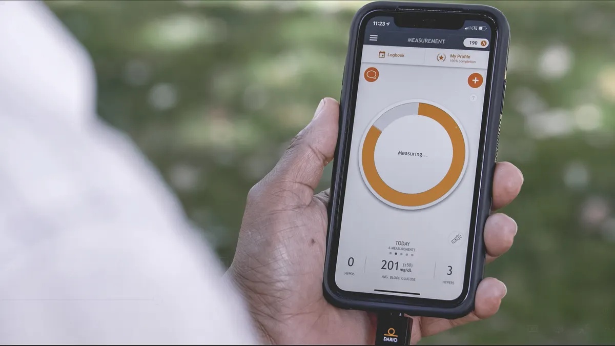 Hands holding a smartphone with the Dario glucose meter connected