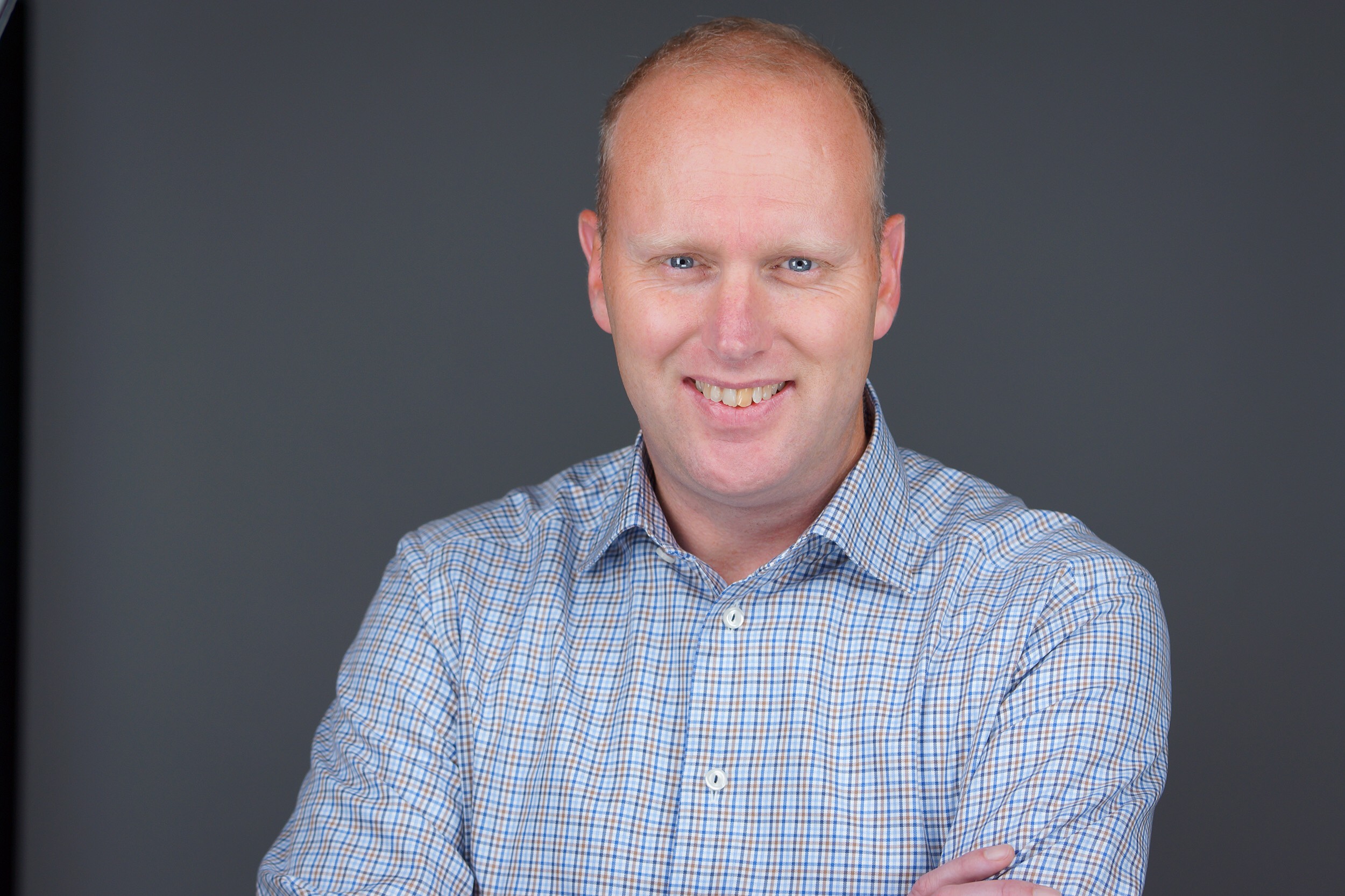 Darren White smiling in a checked shirt in an Aduro press photograph