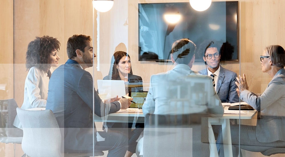 A group of professionals holding a meeting in a glass-walled conference room
