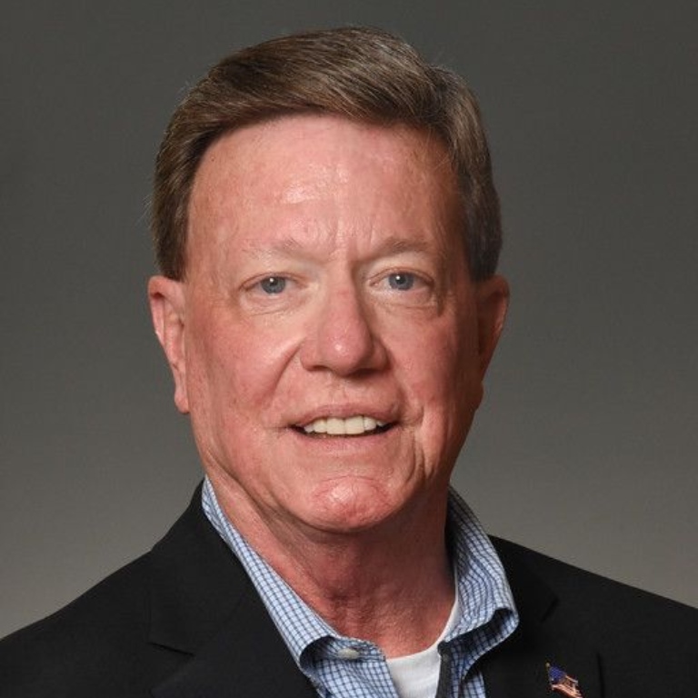 Dave Cook smiling in a dark jacket and checked shirt