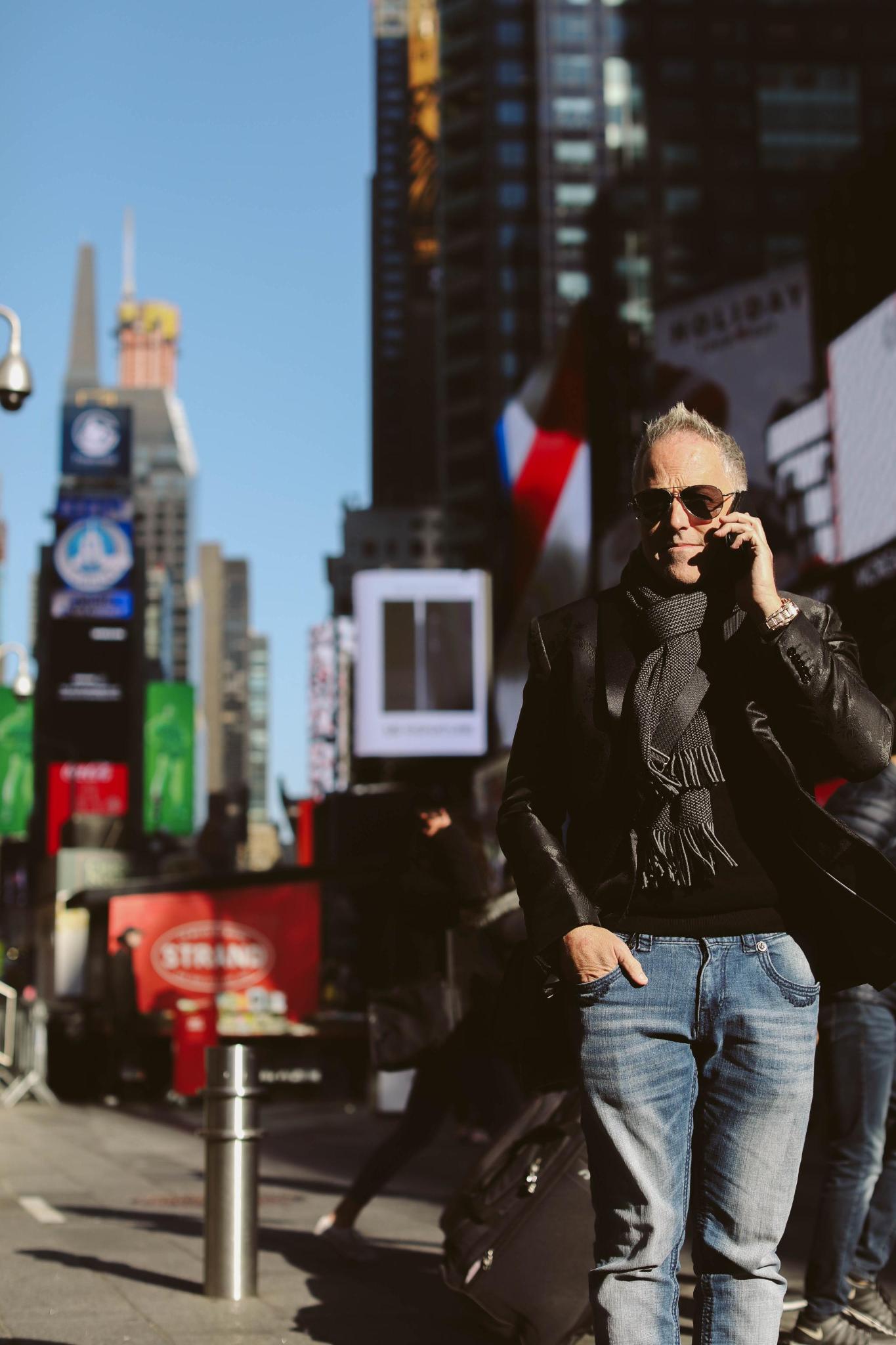 Daven Michaels speaking on a phone in Times Square, wearing a dark jacket and scarf.