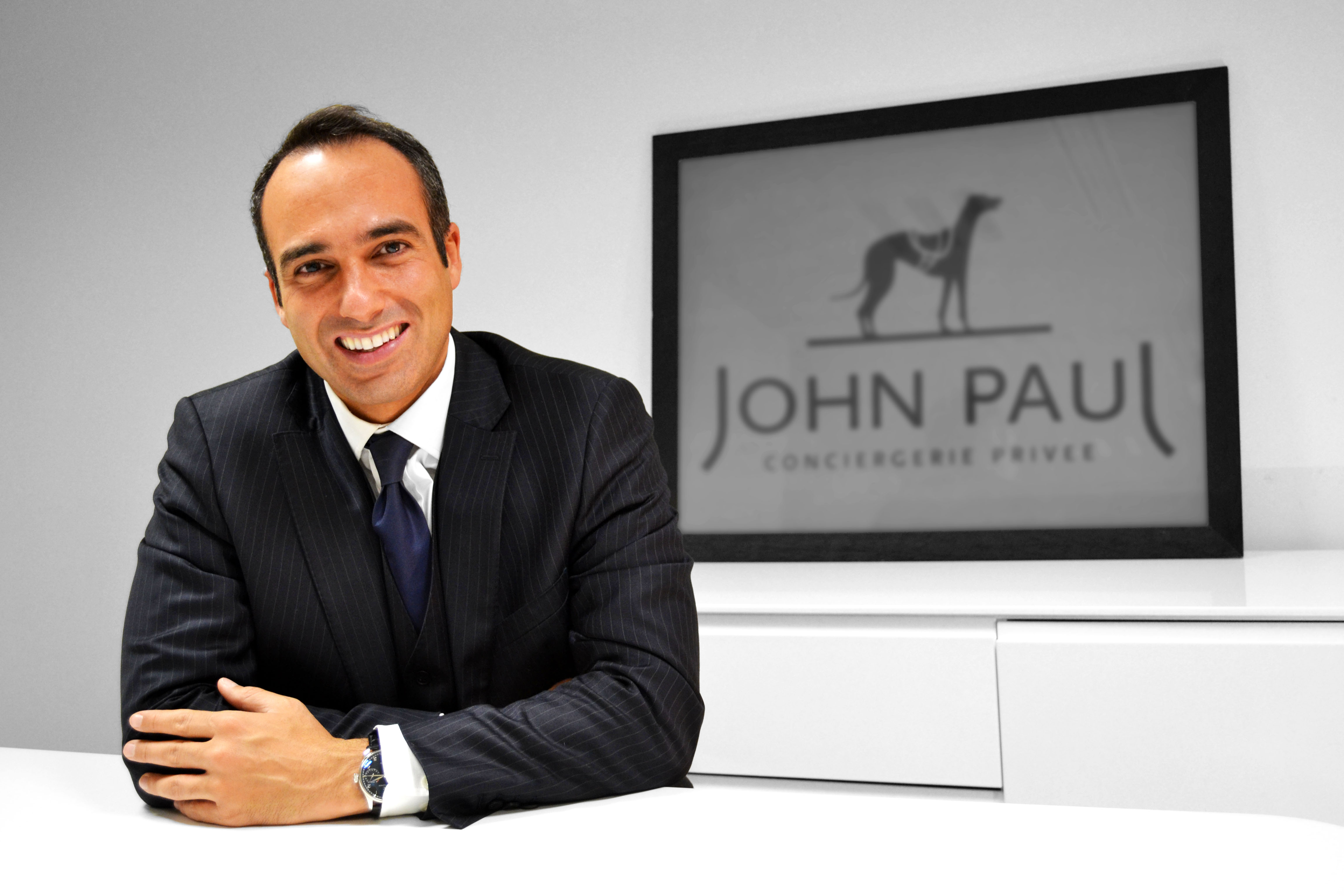 David Amsellem seated at a desk with the John Paul concierge sign behind him