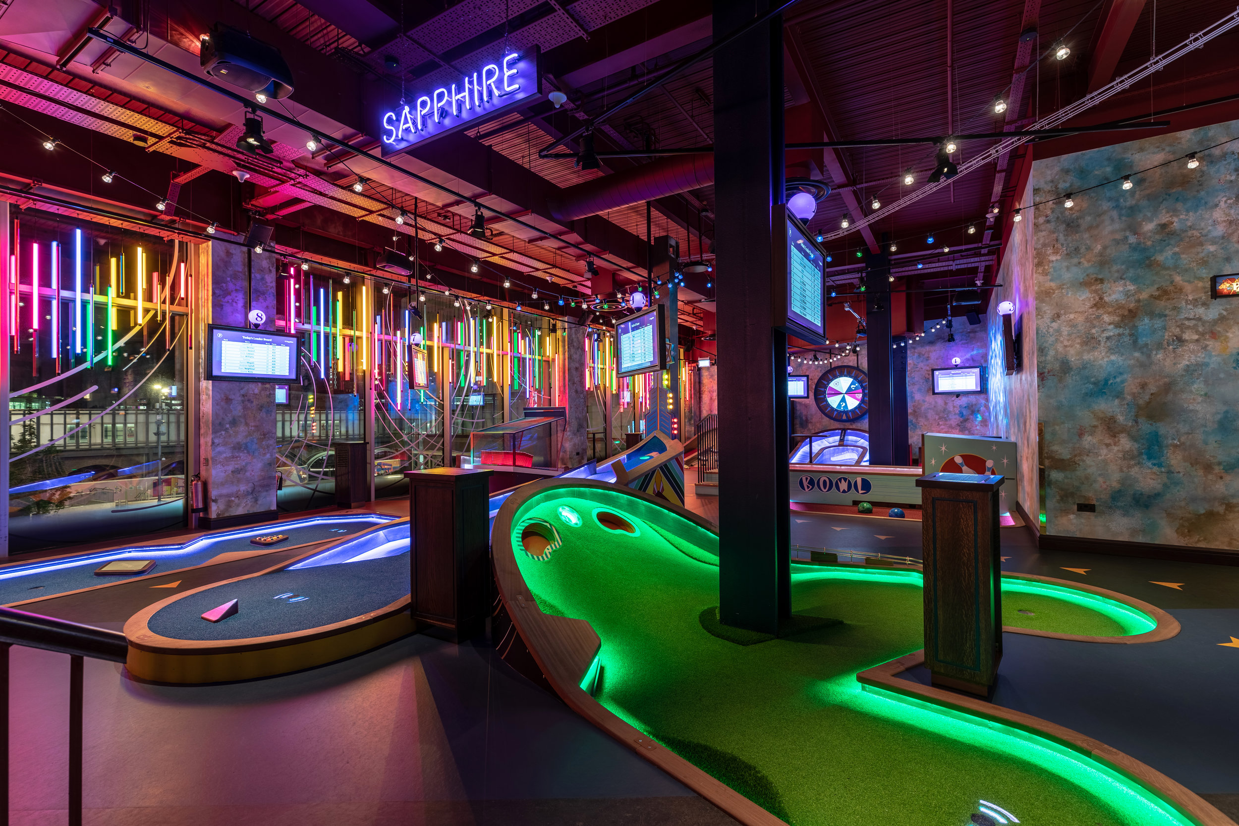 Puttshack interior with illuminated mini golf holes, digital scoreboards and a Sapphire neon sign