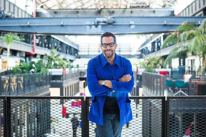 David Belt in a blue jacket on an interior bridge at Newlab, with the industrial structure visible behind him