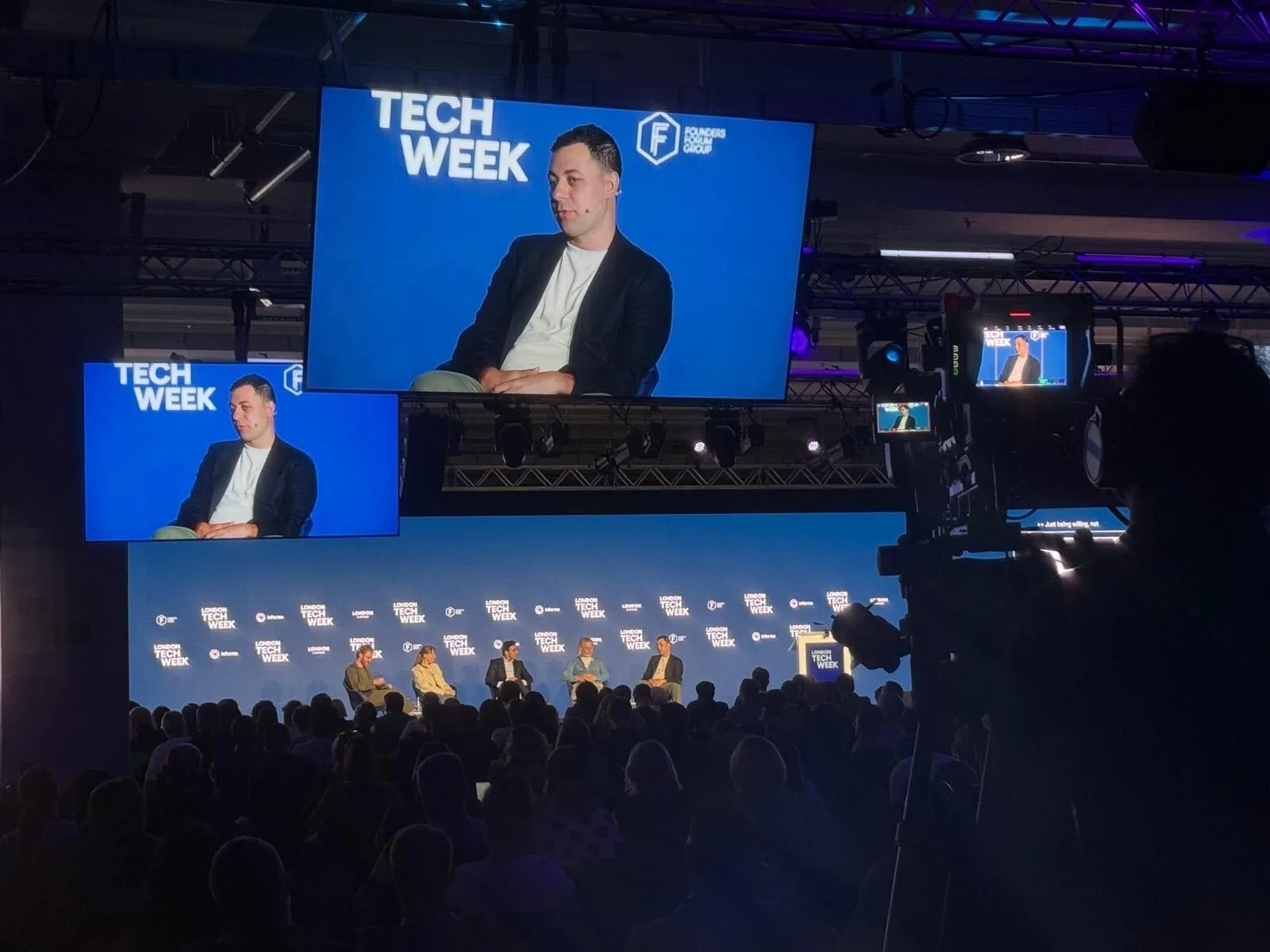 David Casem appears on large screens above a London Tech Week panel and audience