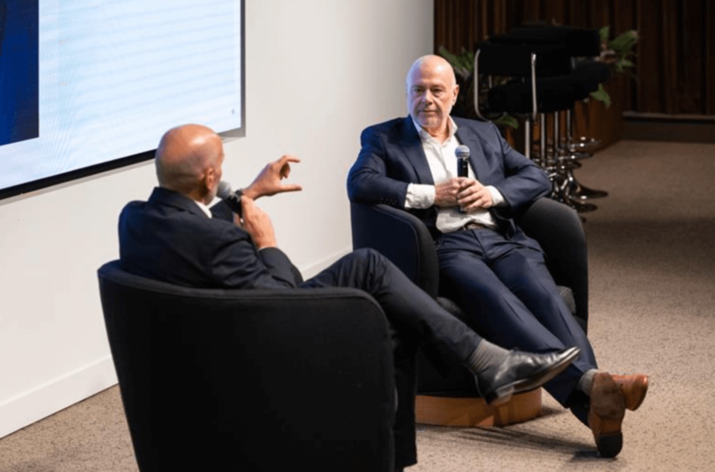 Ed Slack, seated left, interviews David Foulkes, seated right with a microphone, at the IBI Summit in London.