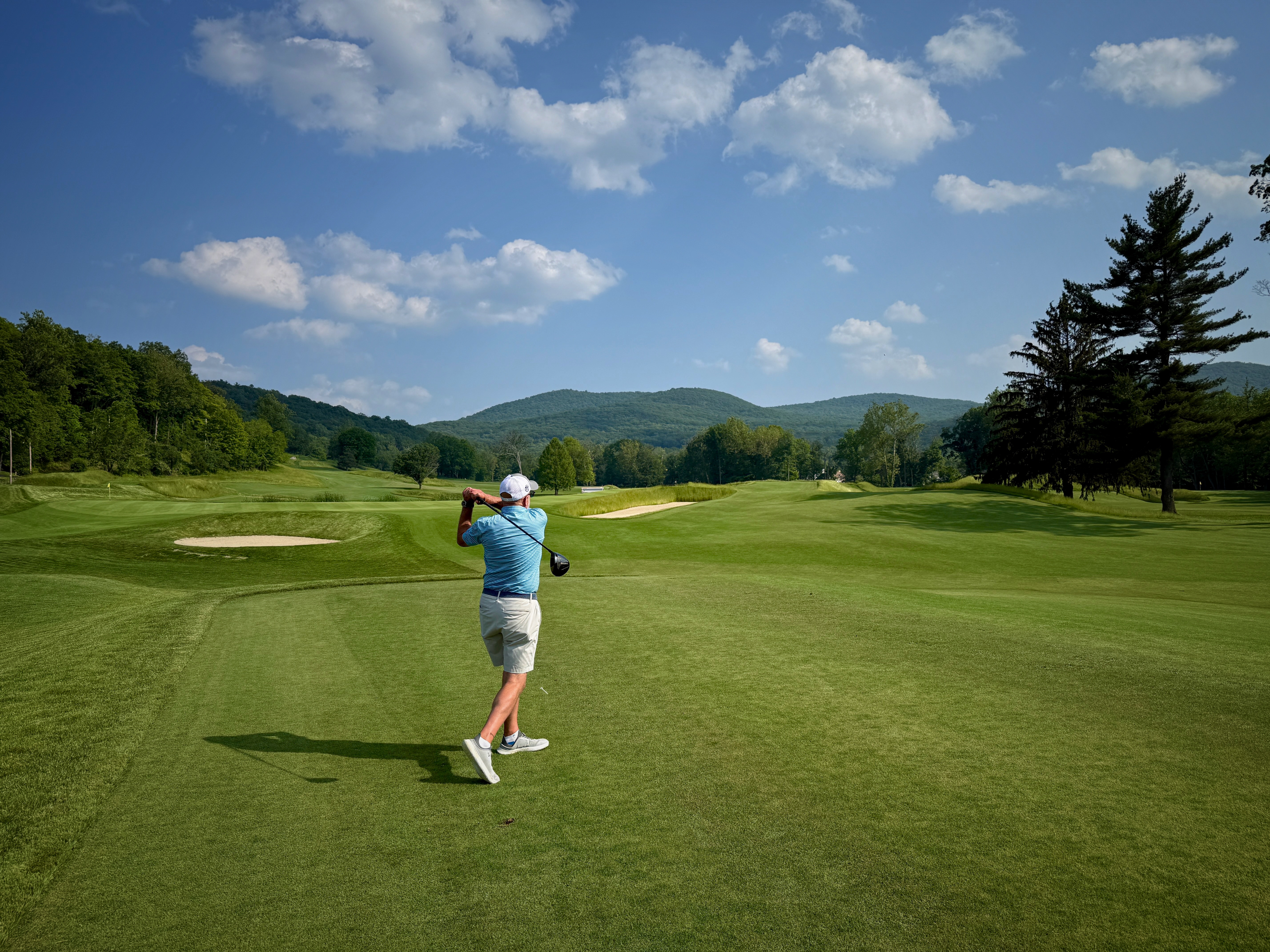 David Gang follows through on a golf shot at Storm King, with hills beyond the fairway