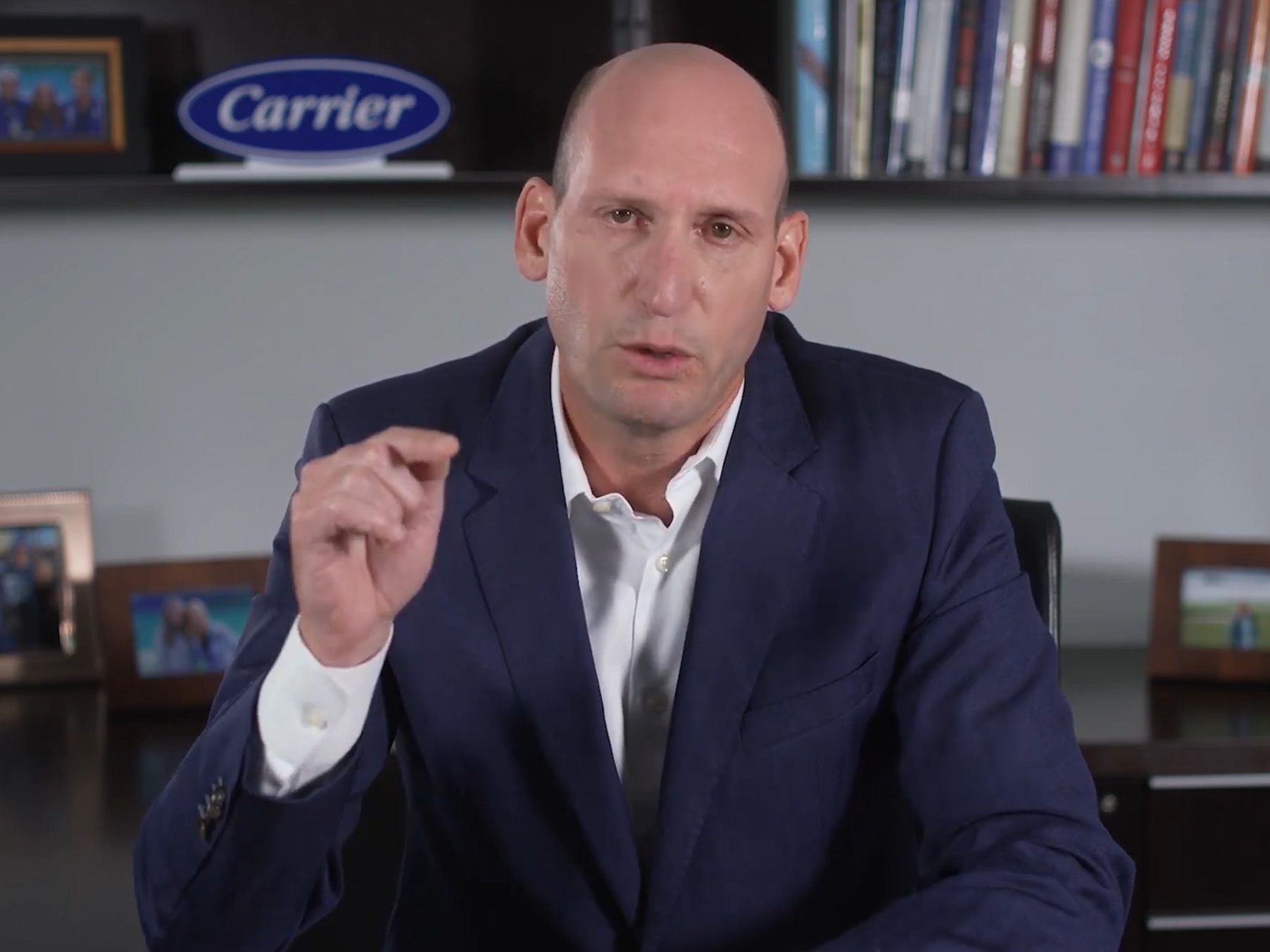 David Gitlin speaking during an interview, gesturing with one hand in front of bookshelves