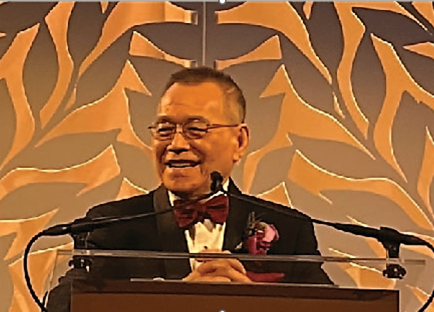 David K. Lam smiling at a lectern, wearing a bow tie and boutonniere