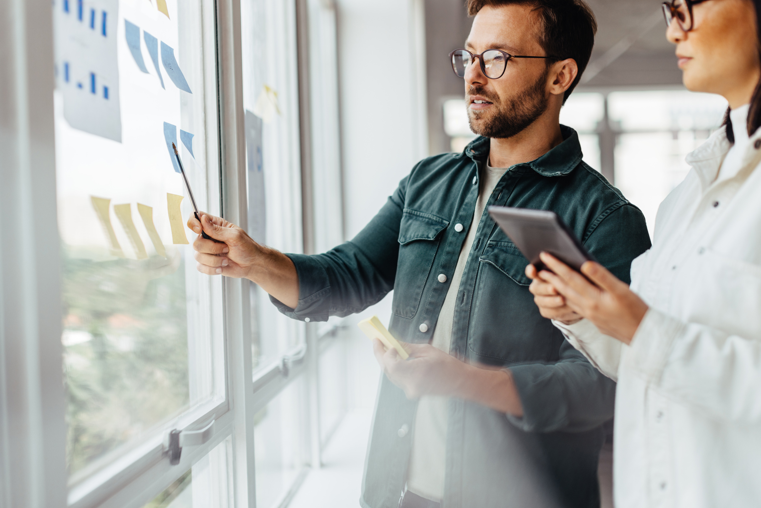 Two colleagues mapping a project with notes on a glass wall