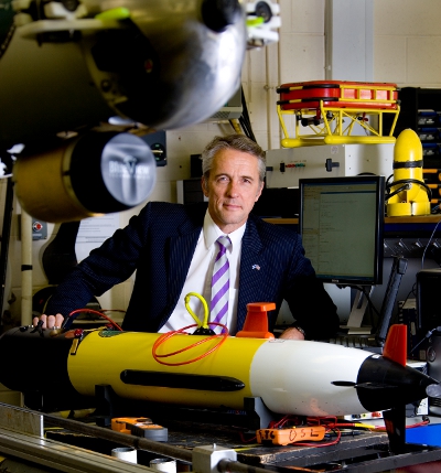 David Lane seated among underwater vehicles and laboratory equipment at the Ocean Systems Laboratory