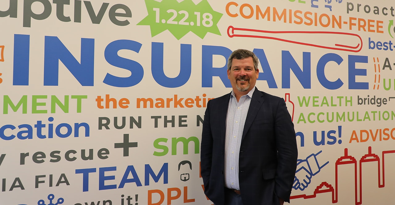 David Lau standing beside a colorful insurance and financial planning word mural