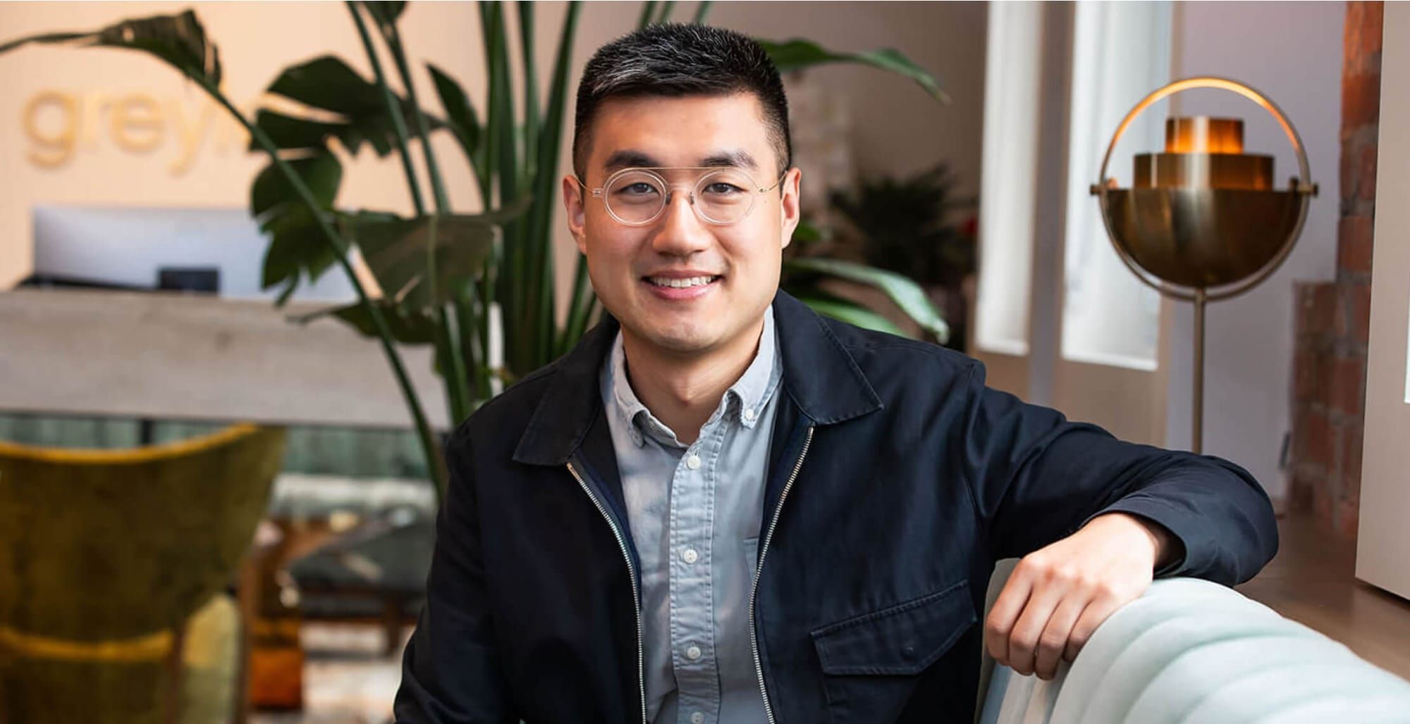 David Luan seated in an office lounge, wearing glasses and a dark jacket